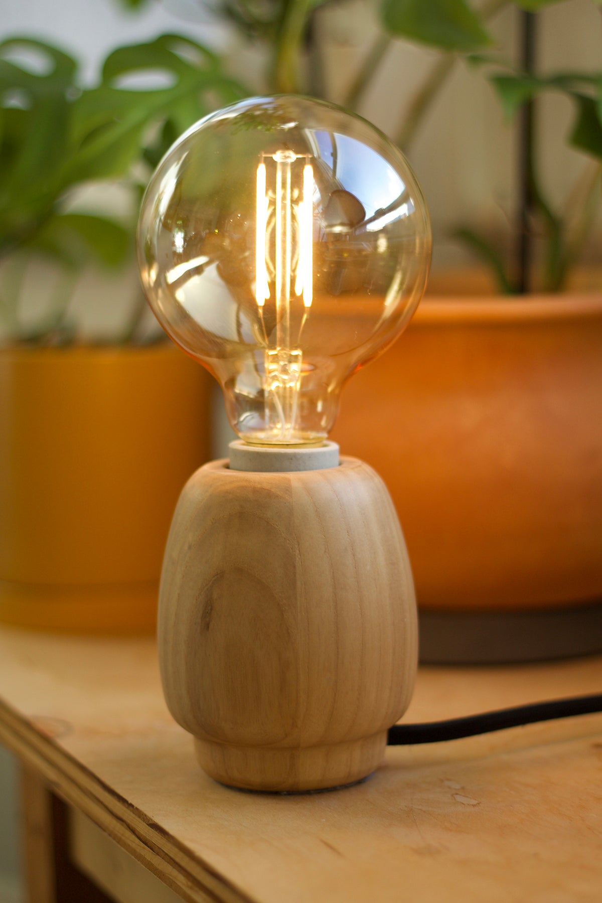 Wooden accent lamp with an Emberline light bulb on a wooden surface with plants in the background