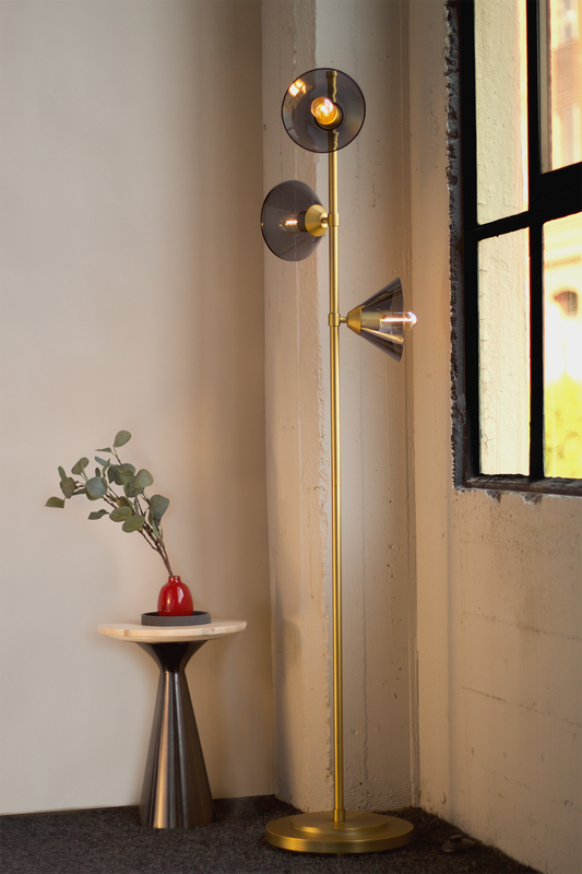 A floor lamp with brass plated steel structure and smoke glass shades, with a red bud vase on a cocktail table in the foreground.