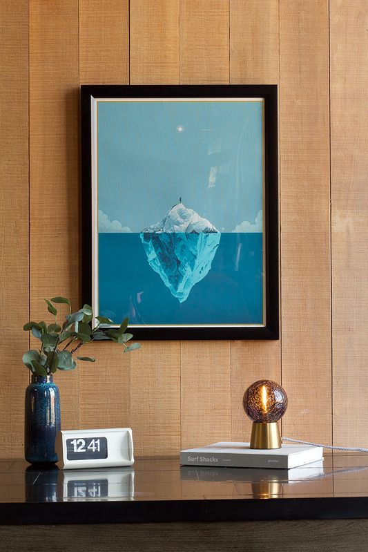 Framed artwork of an iceberg on a wooden wall with decor items and Waverider Accent Lamp below.