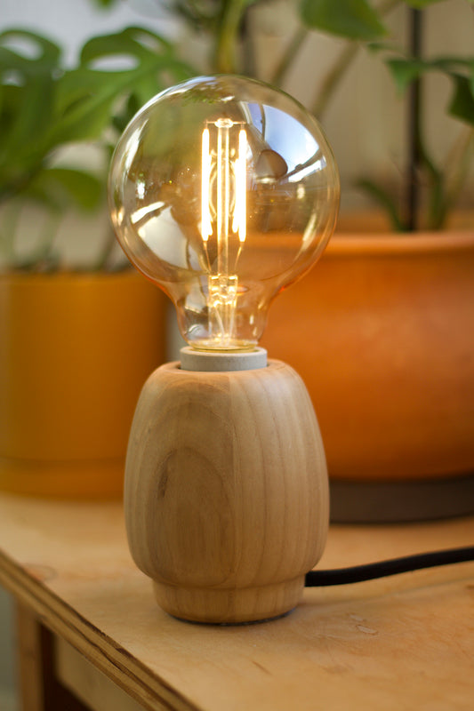 Wooden accent lamp with an Emberline light bulb on a wooden surface with plants in the background