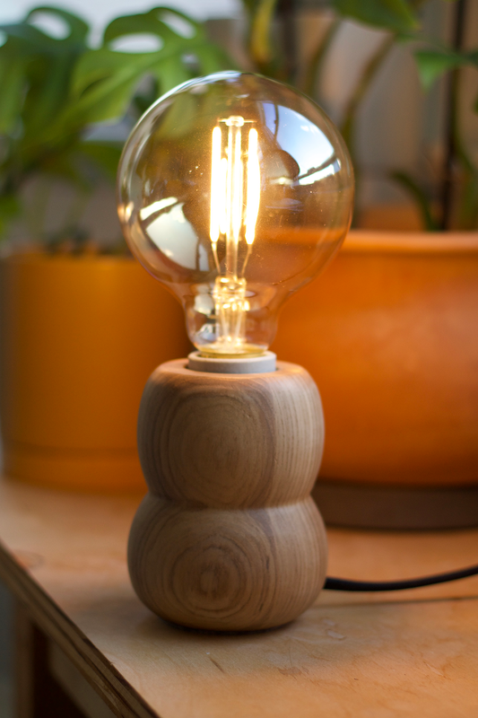 Wooden accent lamp with a vintage-style light bulb on a wooden surface with plants in the background